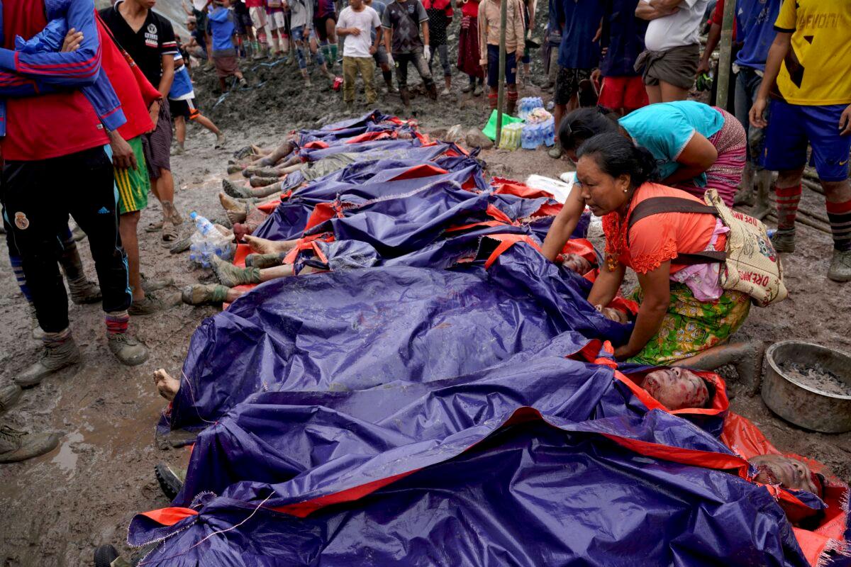 Women look at bodies shrouded in blue and red plastic sheets placed in a row on the ground in Hpakant, Kachin State, Burma, on July 2, 2020. (Zaw Moe Htet/AP Photo)