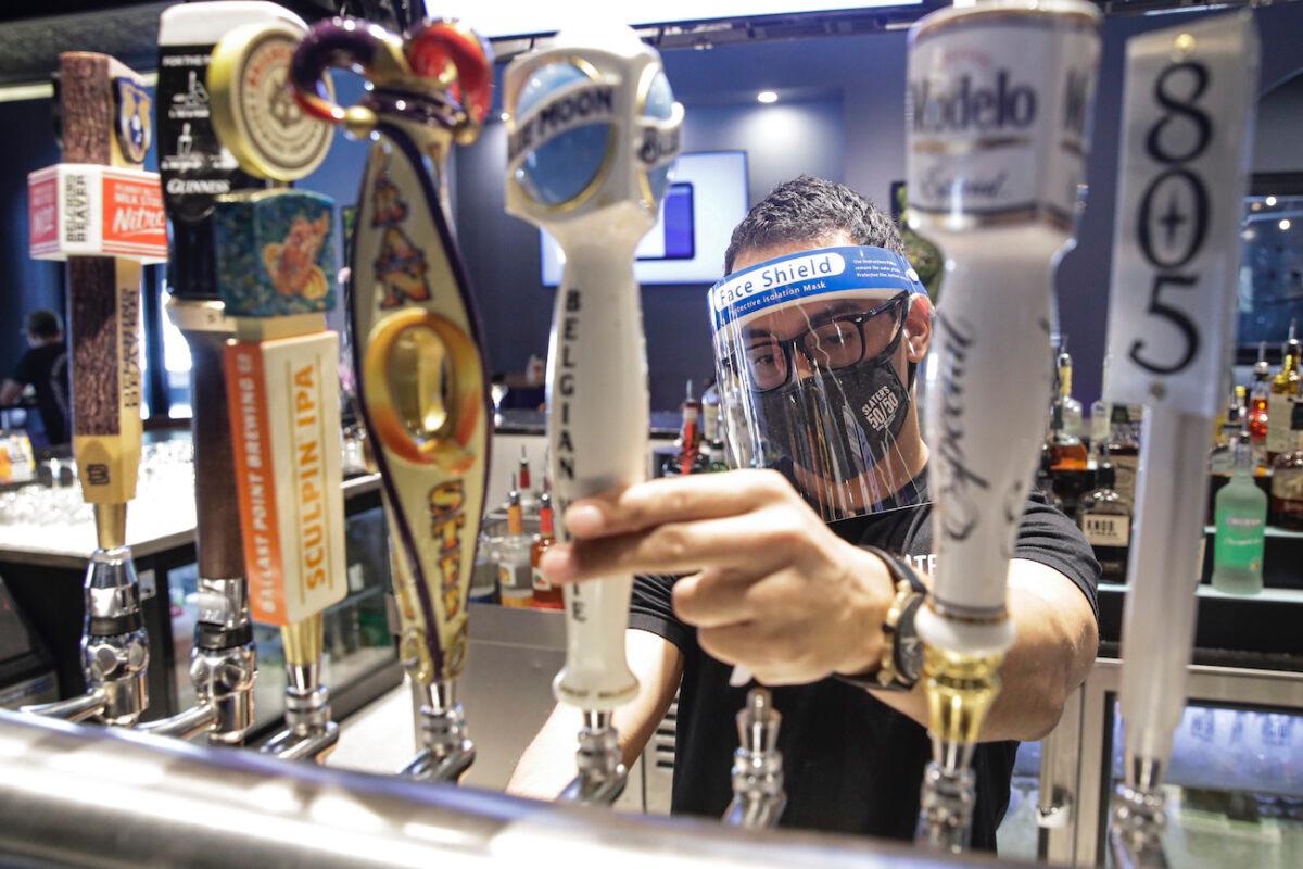 A bartender pours a beer while wearing a mask and face shield amid the COVID-19 pandemic in Santa Clarita, Calif., on July 1, 2020. (AP Photo/Marcio Jose Sanchez)
