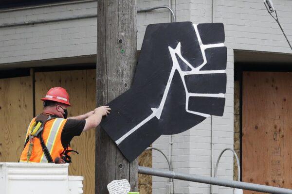A worker removes a rendering of a clenched fist from a Seattle Police precinct in Seattle on July 1, 2020. (Elaine Thompson/AP Photo)
