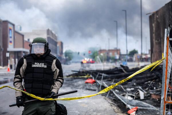 A police officer stands amid smoke and debris as buildings continue to burn in the aftermath of a night of protests and violence following the death of George Floyd, in Minneapolis, on May 29, 2020. (Charlotte Cuthbertson/The Epoch Times)