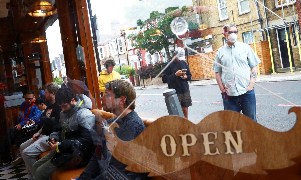 People wait inside and others queue outside Savvas Barbers as it reopened following the outbreak of the coronavirus disease (COVID-19), in London, UK, on July 4, 2020. (Hannah McKay/Reuters)