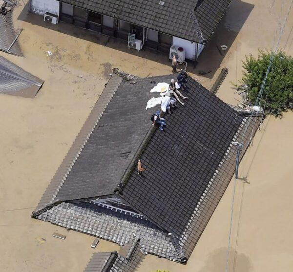 Residents are stranded on the rooftop of a house submerged in muddy waters that gushed out from the Kuma River in Hitoyoshi, Kumamoto prefecture, southwestern Japan on July 4, 2020. (Kyodo News via AP)