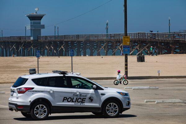 A Seal Beach Police officer drives by a little girl on a bicycle in a closed off parking lot at the Seal Beach Pier area in Seal Beach, Calif., on July 4, 2020. (John Fredricks/The Epoch Times)