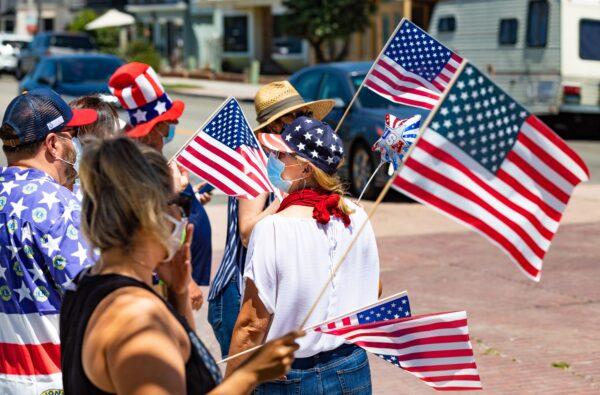 People wave American Flags while wearing masks for protection against COVID-19, in Seal Beach, Calif., on July 4, 2020. (John Fredricks/The Epoch Times)