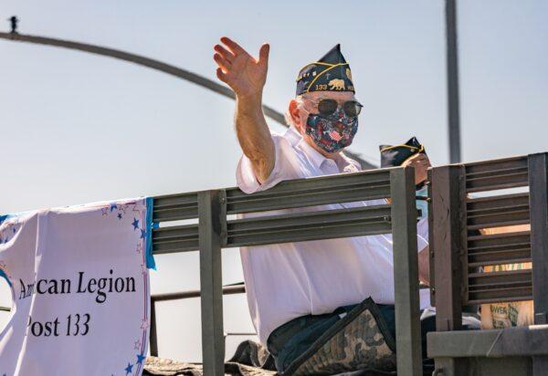 A member of American Legion Post 133 waves from a United States military truck in Huntington Beach, Calif., on July 4, 2020. (John Fredricks/The Epoch Times)