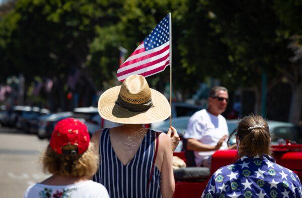 People wave American Flags while wearing masks for protection against COVID-19, in Seal Beach, Calif., on July 4, 2020. (John Fredricks/The Epoch Times)