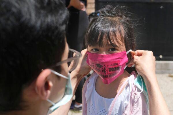 A father helps his daughter with a new mask she received during a graduation ceremony for her Pre-K class in front of Bradford School in Jersey City, N.J., on June 10, 2020. (Seth Wenig/AP)