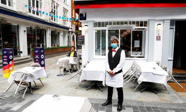 A waiter poses for photographs as he waits for customers outside a restaurant after it reopened following the CCP virus outbreak, in London on July 5, 2020. (Peter Nicholls/Reuters)