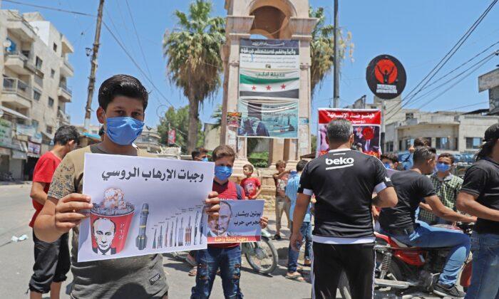 Syrian protesters carry placards expressing their opposition to regime ally Russia's attempt to reduce cross-border aid, as they wear protective masks and maintain social distancing due to the first case of coronavirus recorded a day earlier, in the city of Idlib, Syria, on July 10, 2020. (Abdulaziz Ketaz/AFP/Getty Images)