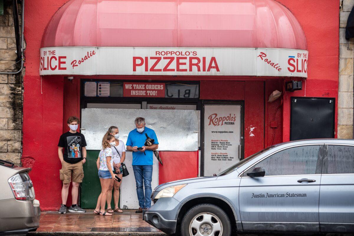 A family wearing facemasks stands in front of a pizzeria in Austin, Texas on June 26, 2020. (Sergio Flores/AFP via Getty Images)