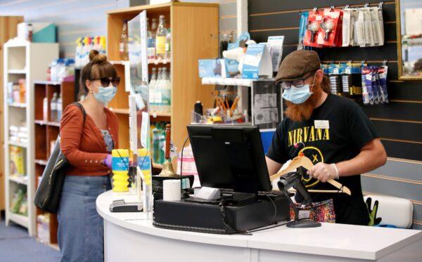 An employee wearing a protective face mask serves a customers at Willen Hospice charity shop in Milton Keynes, Britain, on June 15, 2020. (Andrew Boyers /Reuters)