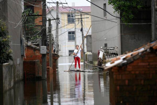 A woman pushes a makeshift raft down a flooded alleyway in a village in Yongxiu in central eastern China's Jiangxi province, on July 16, 2020. (Chinatopix via AP)
