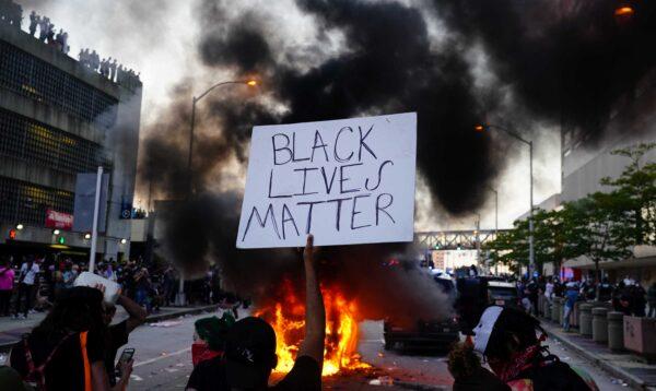 A man holds a Black Lives Matter sign as a police car burns during a protest in Atlanta, Ga., on May 29, 2020. (Elijah Nouvelage/Getty Images)