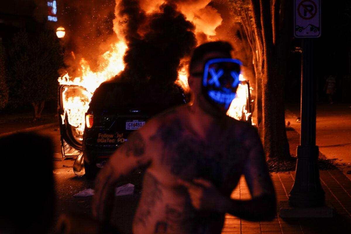 A man wearing a mask runs in front of a burning police car during a riot in Atlanta, Ga., on May 29, 2020. (Elijah Nouvelage/Getty Images)