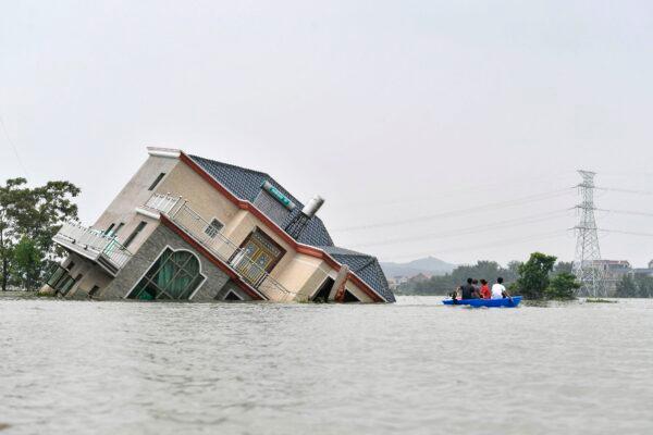 Residents ride a boat past a damaged and flood-affected house near the Poyang Lake due to torrential rains in Poyang county, Shangrao city in China's central Jiangxi province on July 15, 2020. (STR/AFP via Getty Images)