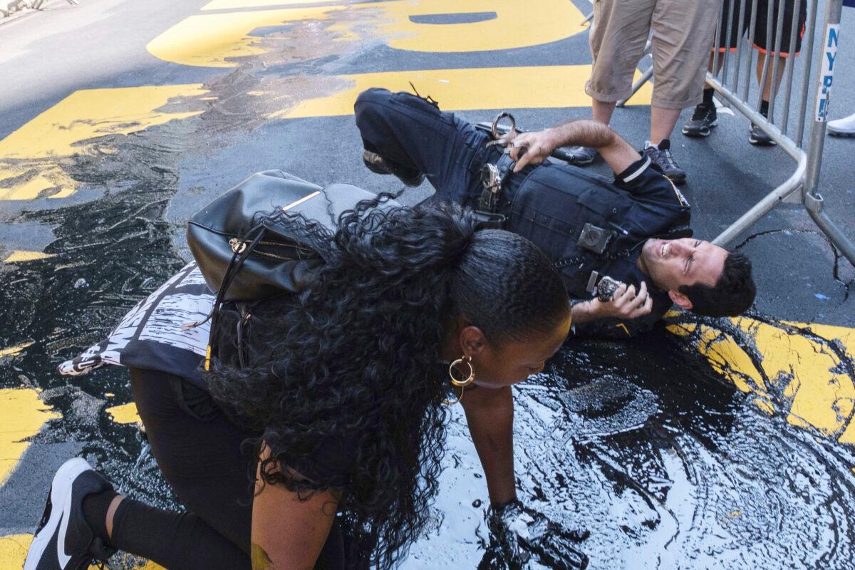 An NYPD officer falls during an attempt to detain a protester pouring black paint on the Black Lives Matter mural outside of Trump Tower on Fifth Avenue in Manhattan on July 18, 2020. (Yuki Iwamura/(AP Photo)