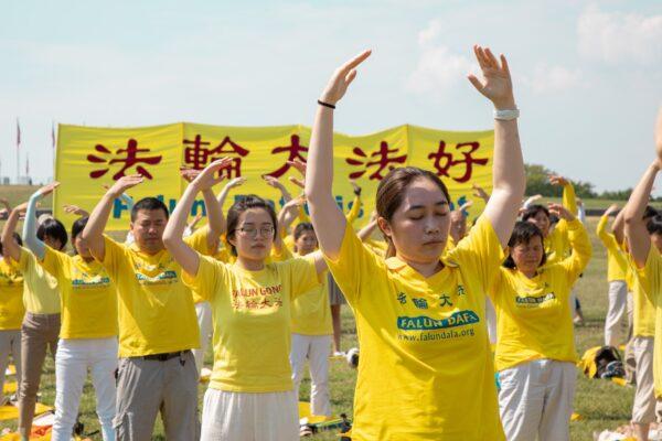 Falun Gong practitioners are practicing exercises on the grass in front of the Washington Monument to urge the stopping of the CCP's persecution of their spiritual discipline, in Washington, D.C., on July 19, 2020. (Lynn Lin/The Epoch Times)