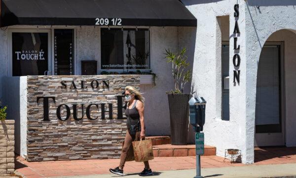 A woman wearing a face mask passes Salon Touche in Redondo Beach, Calif., on July 16, 2020. (John Fredricks/The Epoch Times)