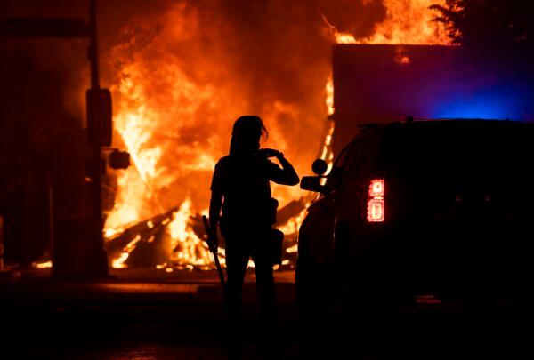 A police officer stands watch as a looted pawn shop burns behind them, in Minneapolis, Minn., on May 28, 2020. (Stephen Maturen/Getty Images)