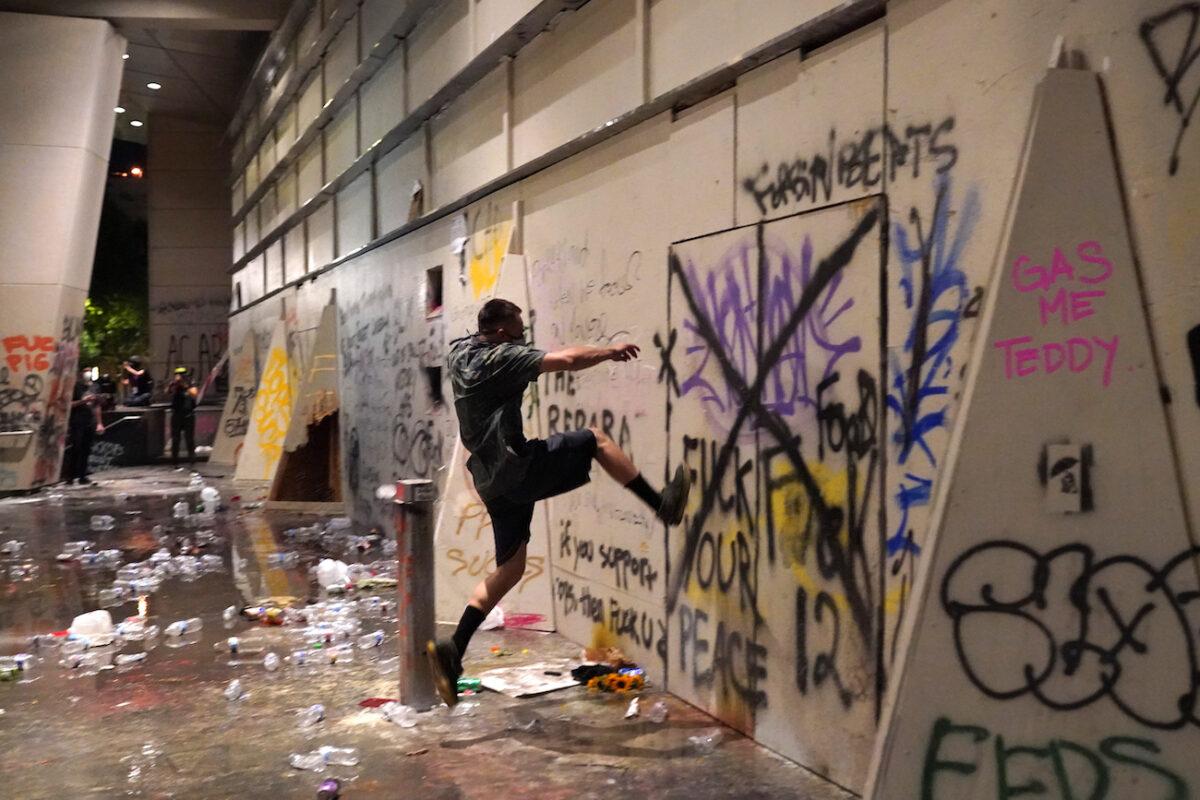 A rioter kicks an entrance to the Mark O. Hatfield Courthouse after federal officers took shelter inside in Portland, Ore., on July 21, 2020. (Nathan Howard/Getty Images)
