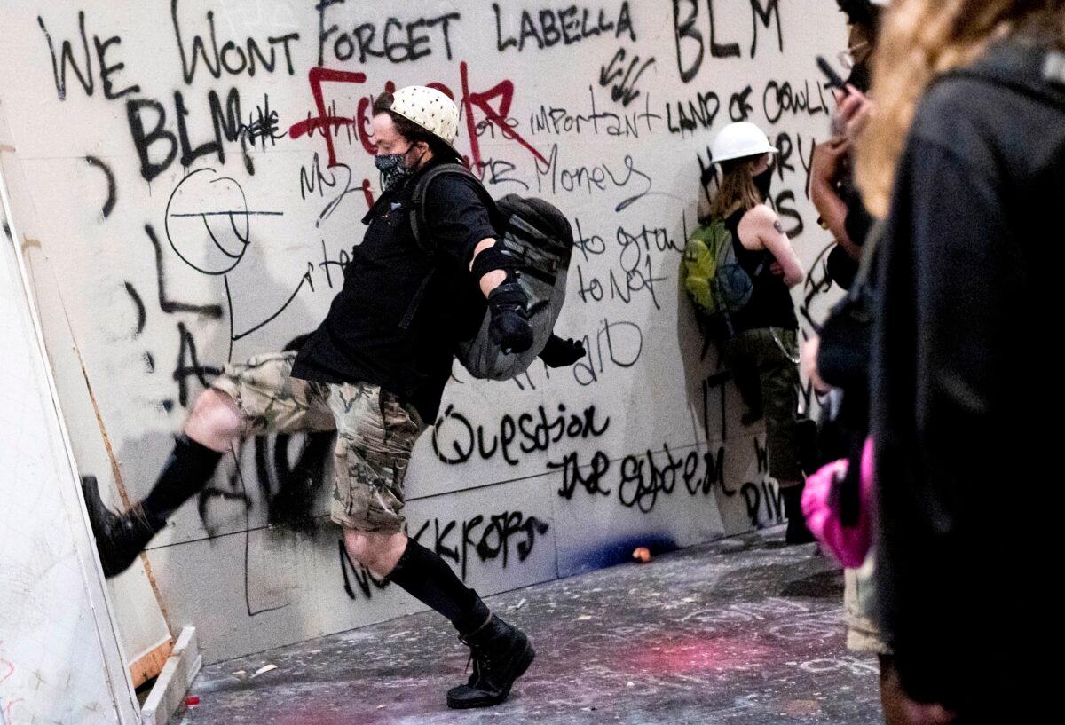 A rioter kicks in temporary boarding at the Mark O. Hatfield United States Courthouse in Portland, Ore., on July 21, 2020. (Noah Berger/AP Photo)