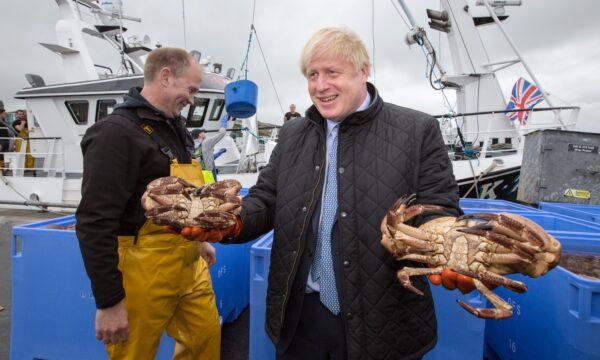 British Prime Minister Boris Johnson holds crabs caught on the Carvela with Karl Adamson at Stromness Harbour, in Stromness, Scotland, on July 23, 2020. (Robert Perry/WPA Pool/Getty Images)