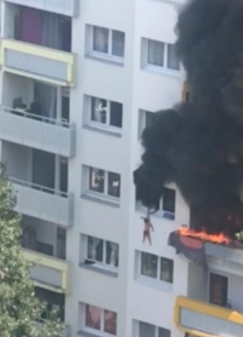 In this grab taken from video, a boy hangs from a window as flames engulf an apartment as onlookers below prepare to catch him in Grenoble, France, Tuesday, July 21, 2020. (AP)