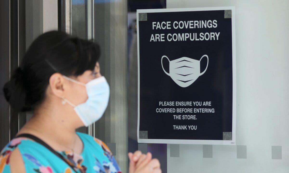 A woman wears a protective mask next to a sign urging to wear face coverings at a store in London on July 24, 2020. (Simon Dawson/Reuters)
