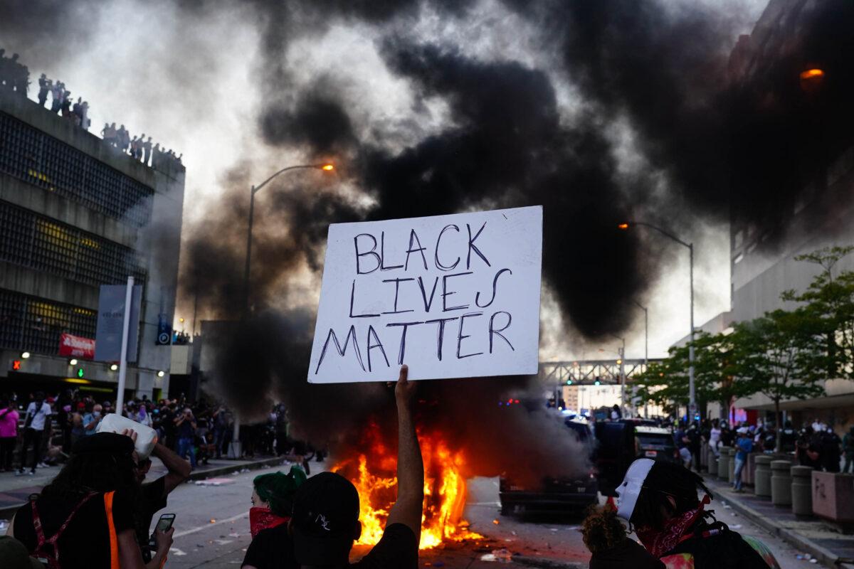 A man holds a Black Lives Matter sign as a police car burns during a protest in Atlanta, Ga., on May 29, 2020. Demonstrations are being held across the U.S. after George Floyd died in police custody on May 25 in Minneapolis, Minn. (Elijah Nouvelage/Getty Images)