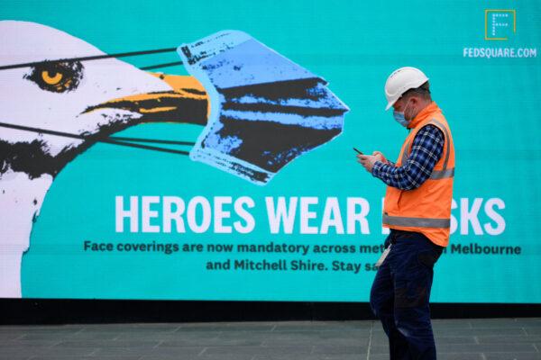 An essential worker wearing a face mask walks past a 'Heroes Wear Masks' sign in Melbourne after it became the first city in Australia to enforce mask-wearing in public as part of efforts to curb a resurgence of the coronavirus disease (COVID-19), on July 23, 2020. (Sandra Sanders/Reuters)