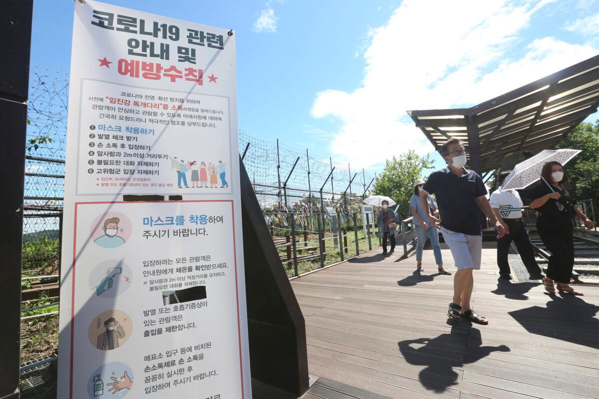 People wearing face masks to help protect against the spread of the new coronavirus pass by a notice about precautions against the coronavirus disease at the Imjingak Pavilion in Paju, South Korea, near the border with North Korea, on July 26, 2020. (Ahn Young-joon/AP Photo)