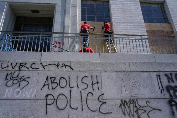 Workers place wooden boards over windows as graffit is shown on walls at the Alameda County Courthouse in Oakland, Calif., on July 26, 2020. (Jeff Chiu/AP Photo)