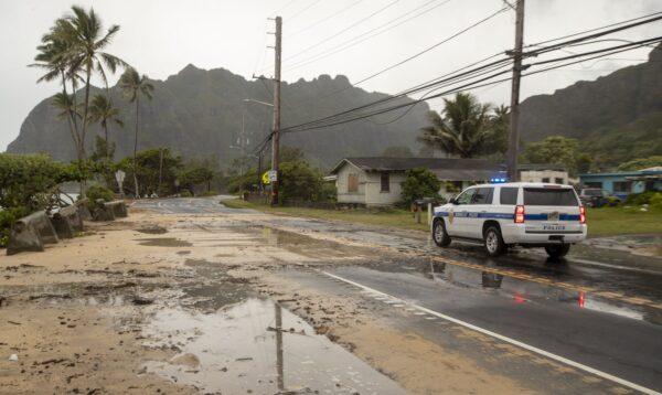 A police officer with the Honolulu Police Department inspects the sand and debris washed onto a closed portion of Kamehameha Highway on July 26, 2020, in Kaaawa, Hawaii. (Eugene Tanner/AP Photo)