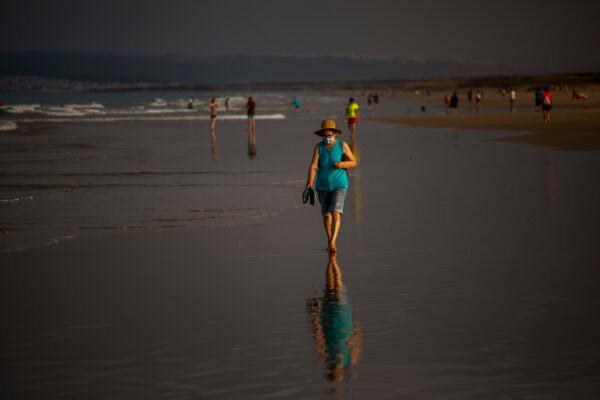 A woman wearing a mask walks on the beach in Zahara de los Atunes, Cadiz province, south of Spain, July 25, 2020. (Emilio Morenatti/AP Photo)