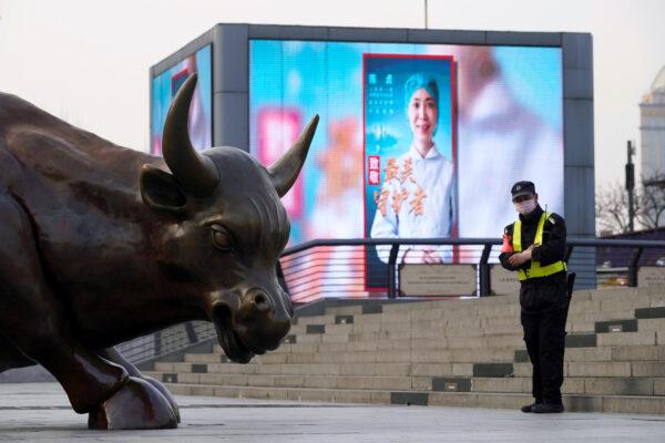 A security guard wearing a face mask stands near the Bund Financial Bull statue and a display showing an image of a medical worker following the novel coronavirus disease (COVID-19) outbreak, on The Bund in Shanghai on March 18, 2020. (Aly Song/Reuters)
