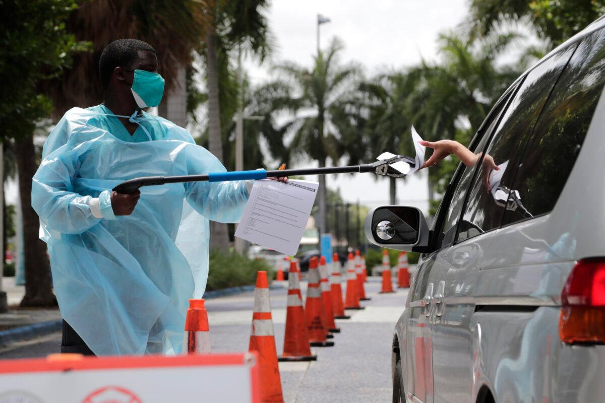 Healthcare worker Dante Hills (L) passes paperwork to a woman in a vehicle at a COVID-19 testing site outside of Marlins Park, in Miami, Fla., on July 27, 2020. (Lynne Sladky/AP Photo)