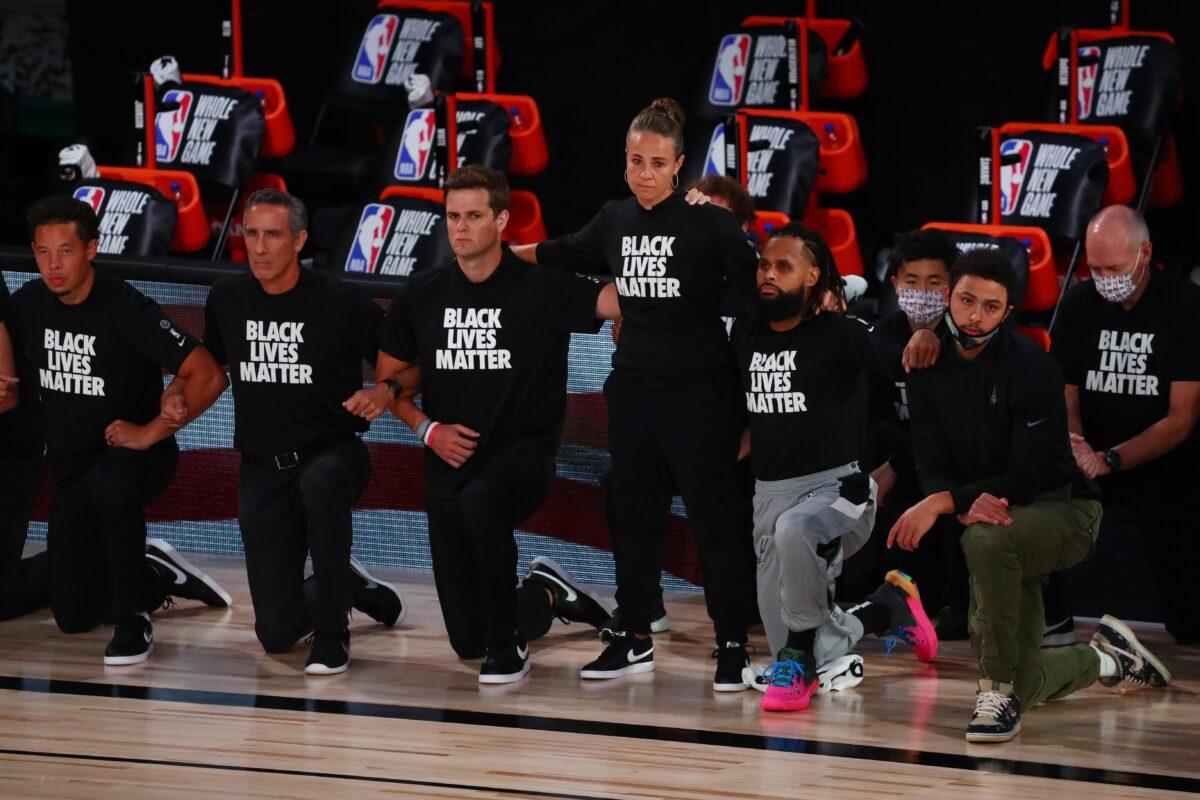 Assistant coach Becky Hammon of the San Antonio Spurs stands as other players and staff kneel before an NBA basketball game at the Visa Athletic Center in Lake Buena Vista, Fla., on July 31, 2020. (Kim Klement/Pool/Getty Images)