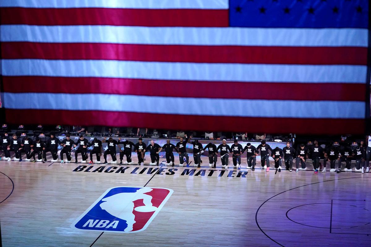 Members of the Orlando Magic and Brooklyn Nets kneel around a Black Lives Matter logo during the national anthem before the start of an NBA basketball game Friday, July 31, 2020, in Lake Buena Vista, Fla. (Ashley Landis, Pool/AP Photo)