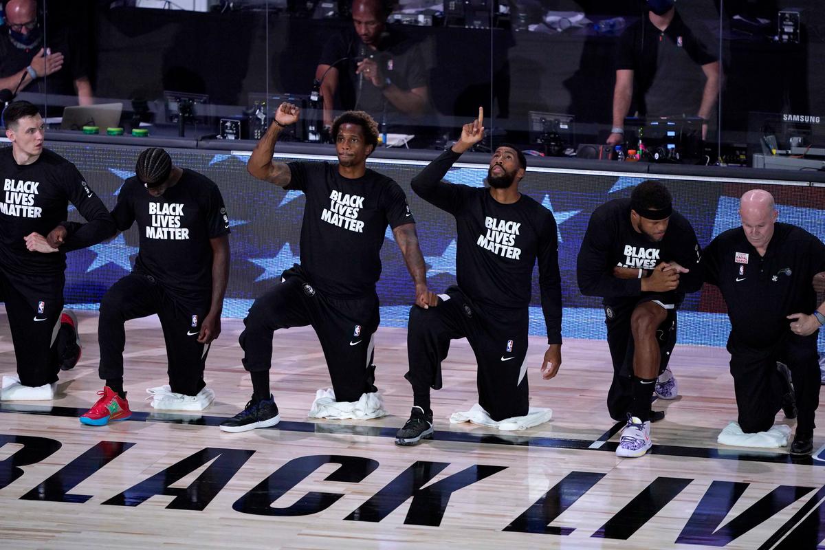 Players kneel and wear Black Lives Matter shirts as the pause before the start of an NBA basketball game between the Brooklyn Nets and the Orlando Magic Friday, July 31, 2020, in Lake Buena Vista, Fla. (Ashley Landis, Pool/AP Photo)