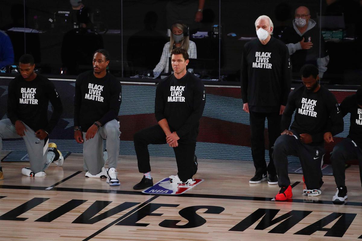 San Antonio Spurs head coach Gregg Popovich, fourth from left, stands while wearing a mask while Sacramento Kings head coach Luke Walton, center, kneels with players before an NBA basketball game Friday, July 31, 2020, in Lake Buena Vista, Fla. (Kim Klement/Pool Photo via AP)