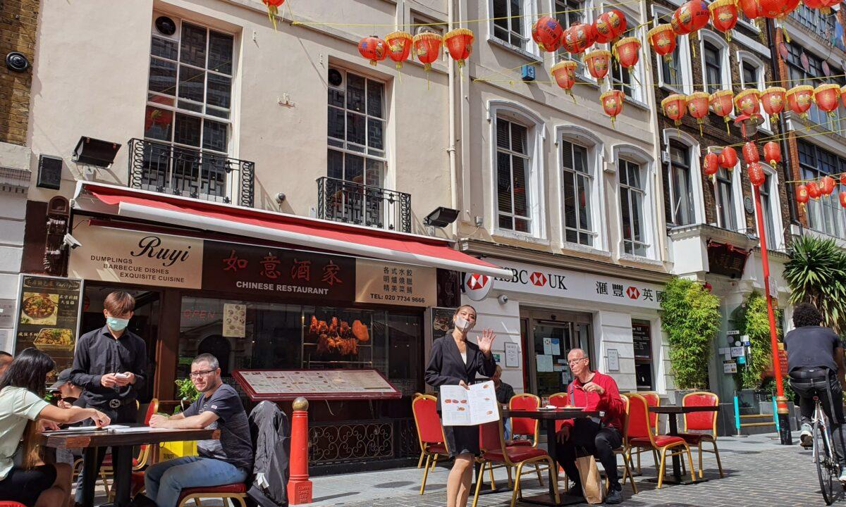 A Chinese restaurant employee tries to entice customers to eat at her restaurant, which has started to put out tables on the street as part of its social distancing efforts, in China Town, London, Britain, on July 26, 2020. (Lily Zhou/The Epoch Times)