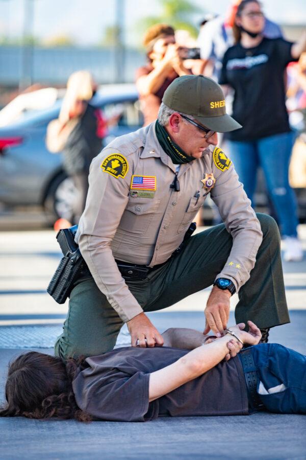 An officer kneels on the ground beside a protester as he arrests the protester in Yucaipa, Calif., on Aug. 1, 2020. (John Fredricks/The Epoch Times)