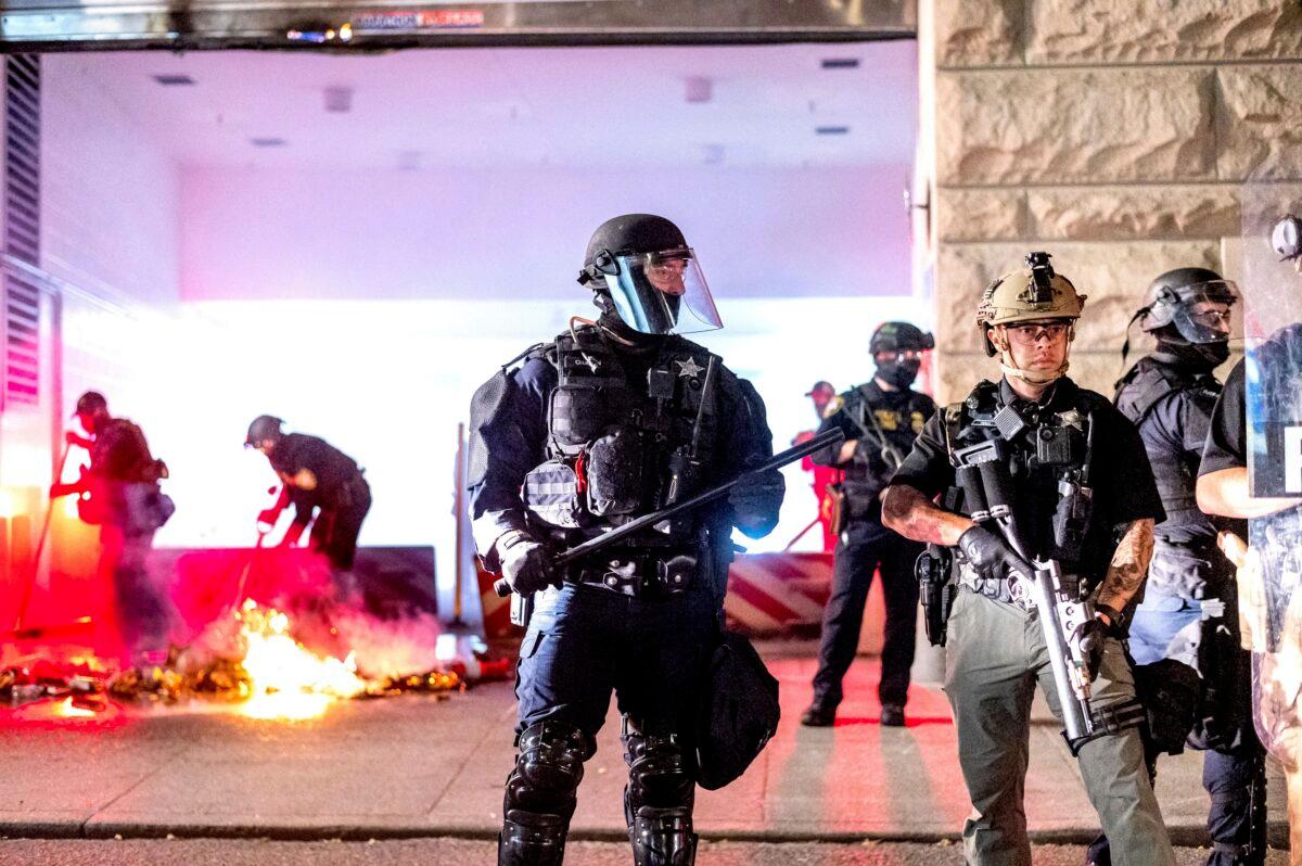 An Oregon State Police officer, right, stands watch as officers extinguish a fire lit by protesters behind the Mark O. Hatfield United States Courthouse in Portland, Ore., on Aug. 2, 2020. (Noah Berger/AP Photo)