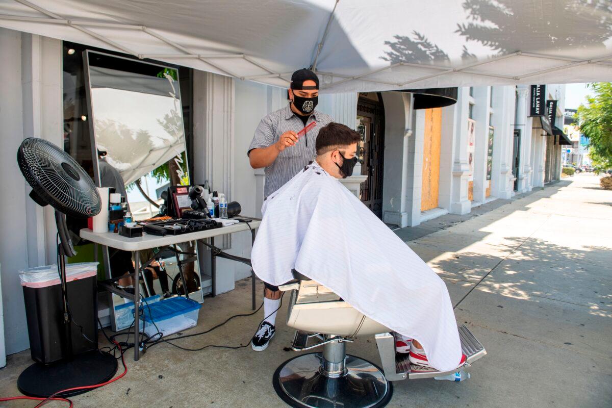 A stylist from Grey Matter LA cuts a client's hair, both wearing facemasks, amid the COVID-19 pandemic, in Los Angeles, on Aug. 4, 2020. (Valerie Macon/AFP via Getty Images)