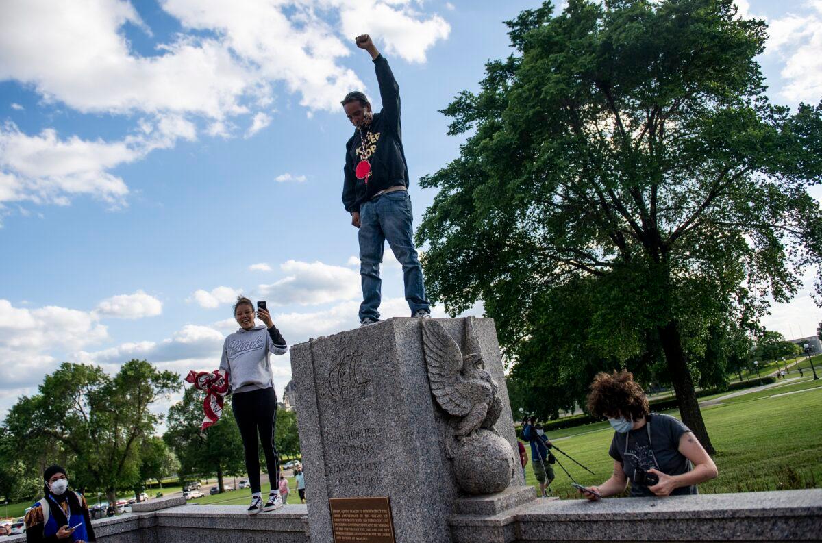 A man stands with his fist raised on the spot where a statue of Christopher Columbus was toppled by vandals on the grounds of the State Capitol in St Paul, Minn., on June 10, 2020. (Stephen Maturen/Getty Images)