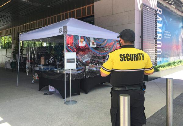 A security staff member stands near a booth at the open-air mall. (Ilene Eng/The Epoch Times)