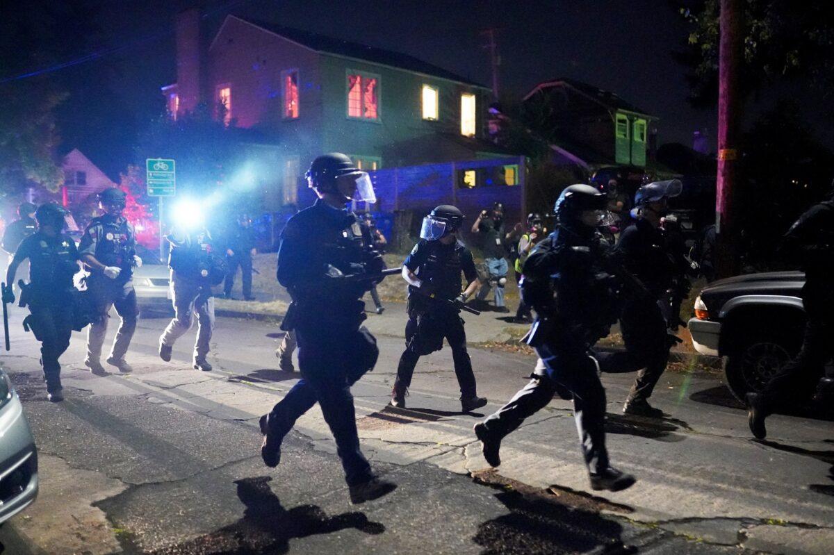 Portland police run through a residential neighborhood while dispersing a crowd of about 400 rioters in Portland, Ore., on Aug. 14, 2020. (Nathan Howard/Getty Images)