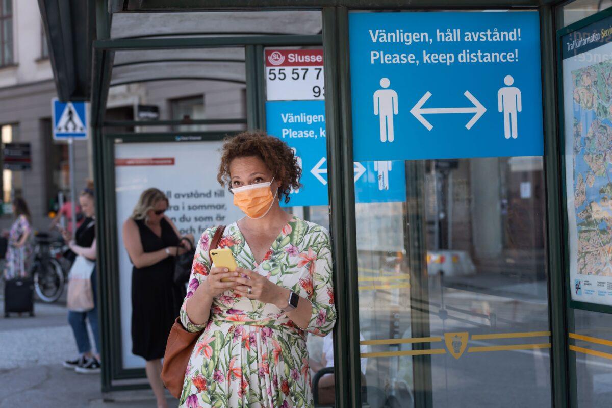A woman wearing a mask waits at a bus stop in Stockholm, on June 26, 2020. (Stina Stjernkvist/TT News Agency/AFP via Getty Images)
