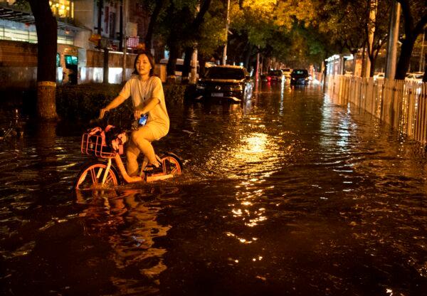 A woman uses a bike to cross a flooded street after a sudden rain in Beijing on Aug. 9, 2020. (NOEL CELIS/AFP via Getty Images)