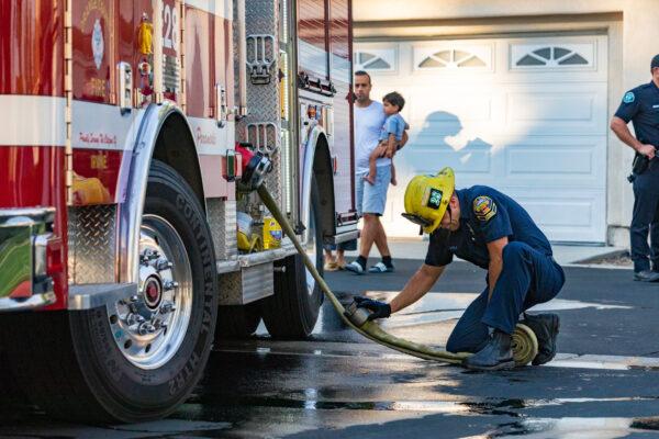 A firefighter with the Orange County Fire Department connects a hose to the truck while bystanders look on in Irvine, Calif., on Aug. 17, 2020. (John Fredricks/The Epoch Times)